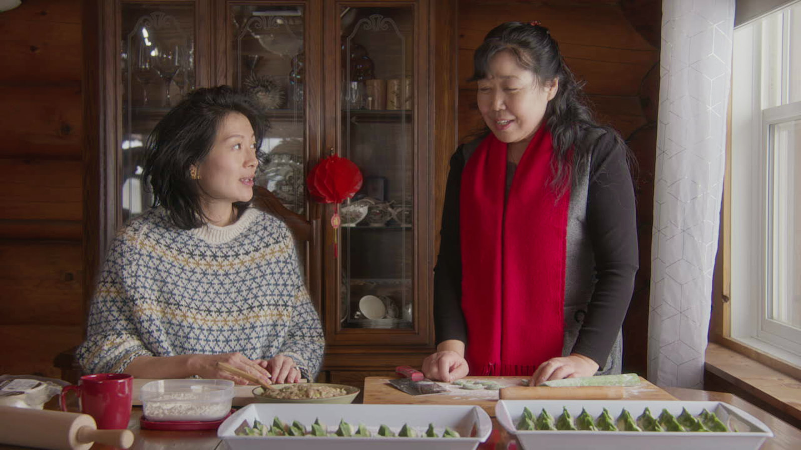 Jackie Kai Ellis making dumplings with a guest at a kitchen table