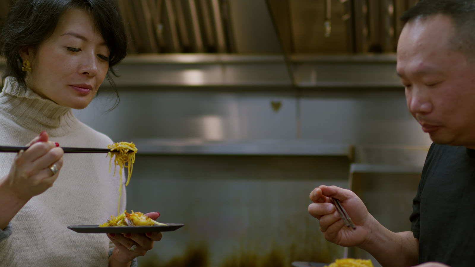 Jackie Kai Ellis sharing a plate of noodles with a chef