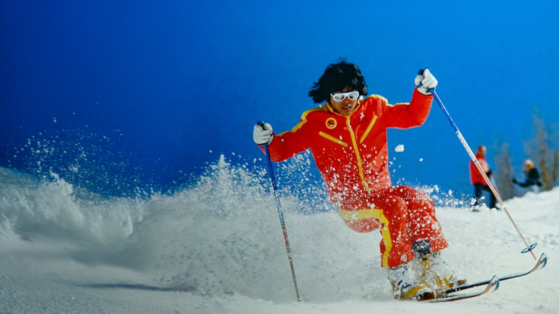 Archival photograph of Wayne Wong skiing in a bright red suit beneath a blue sky